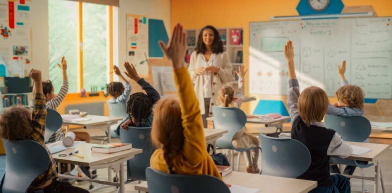 Children in a classroom with their hands raised facing the teacher