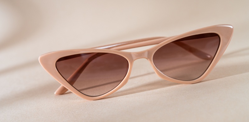 A pair of peach colored, cat eye sunglasses on a neutral surface