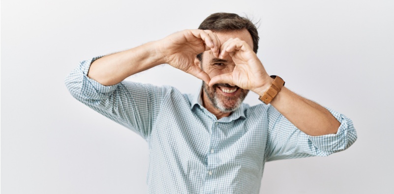 A man creating a heart with his hands over his eye.]