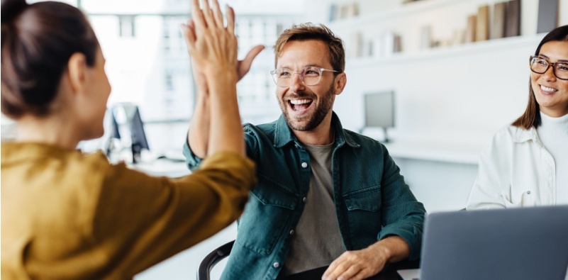 An office worker wearing glasses, giving a high-five to his colleague.