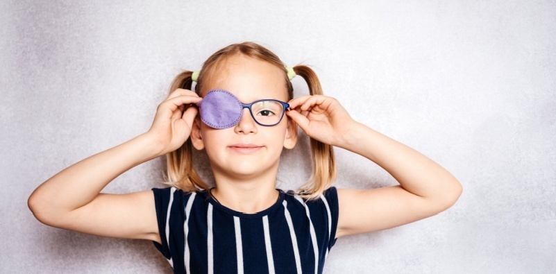 A young girl wearing eyeglasses and an eye patch over her right eye