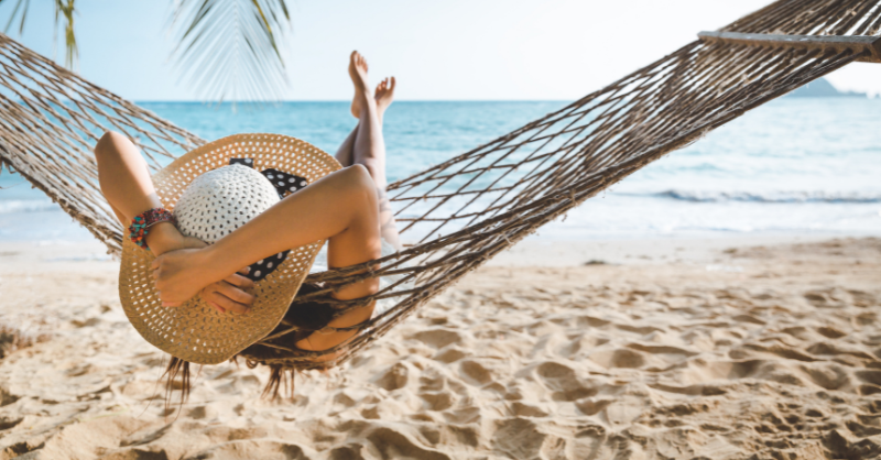 A woman in a hammock, wearing a hat facing the sea.