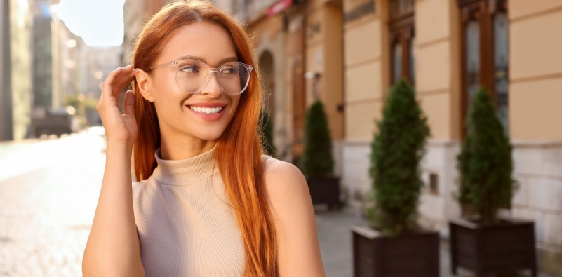 A red-haired woman wearing transparent glasses, outdoors