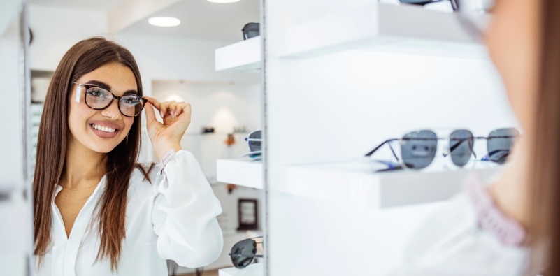 A young woman trying on a new pair of glasses at the eye doctor’s office trying to decide which pair fits best.