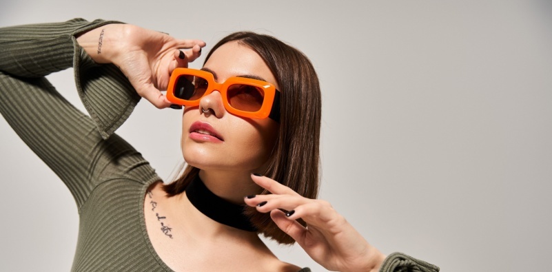 A young woman with brunette hair, wearing a green shirt and orange sunglasses.